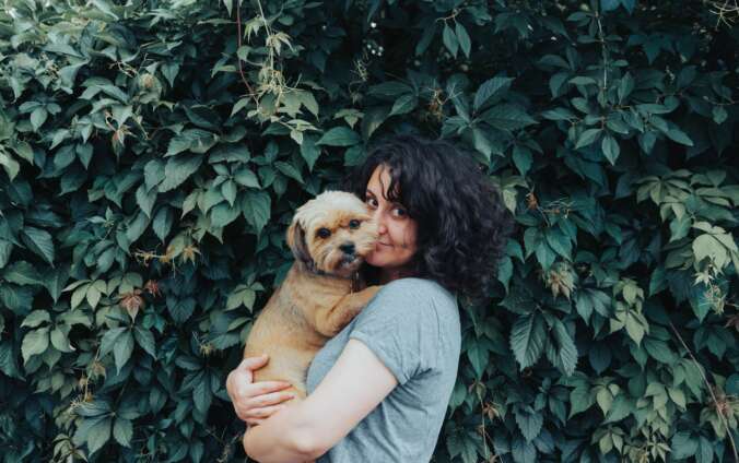 A woman cuddles her golden pup near a green hedge